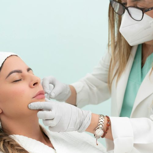 Doctor performing cosmetic treatment on a woman with eyes closed in a clinical setting.